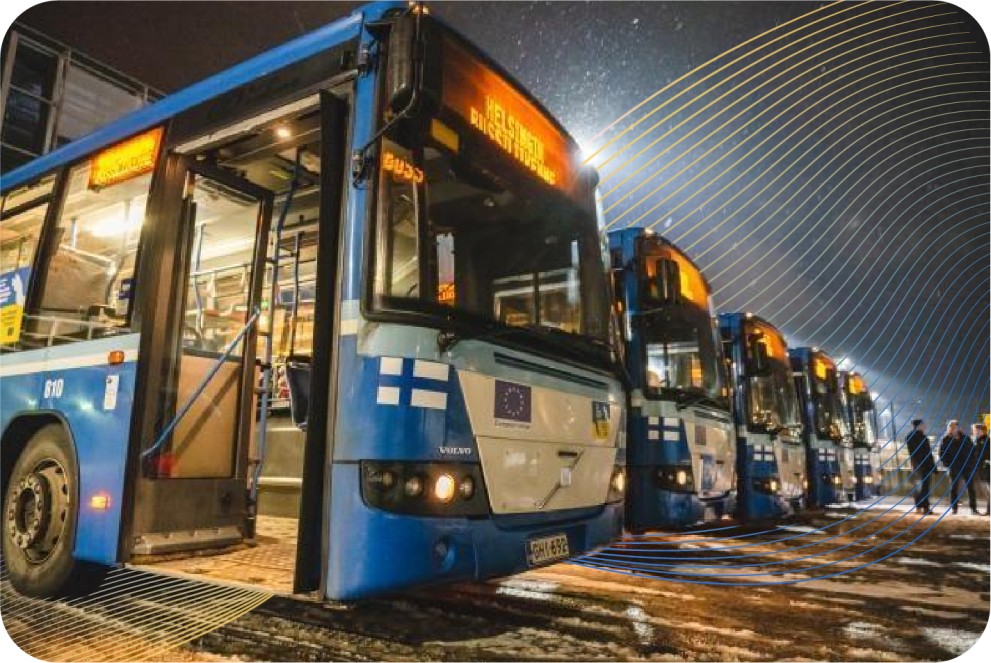 Blue school buses from Finland parked in a row at nighttime. 